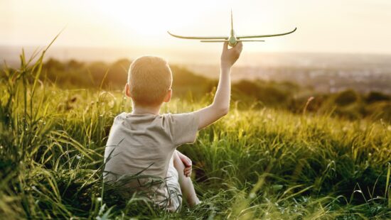 Little boy sitting on the meadow with toy airplane